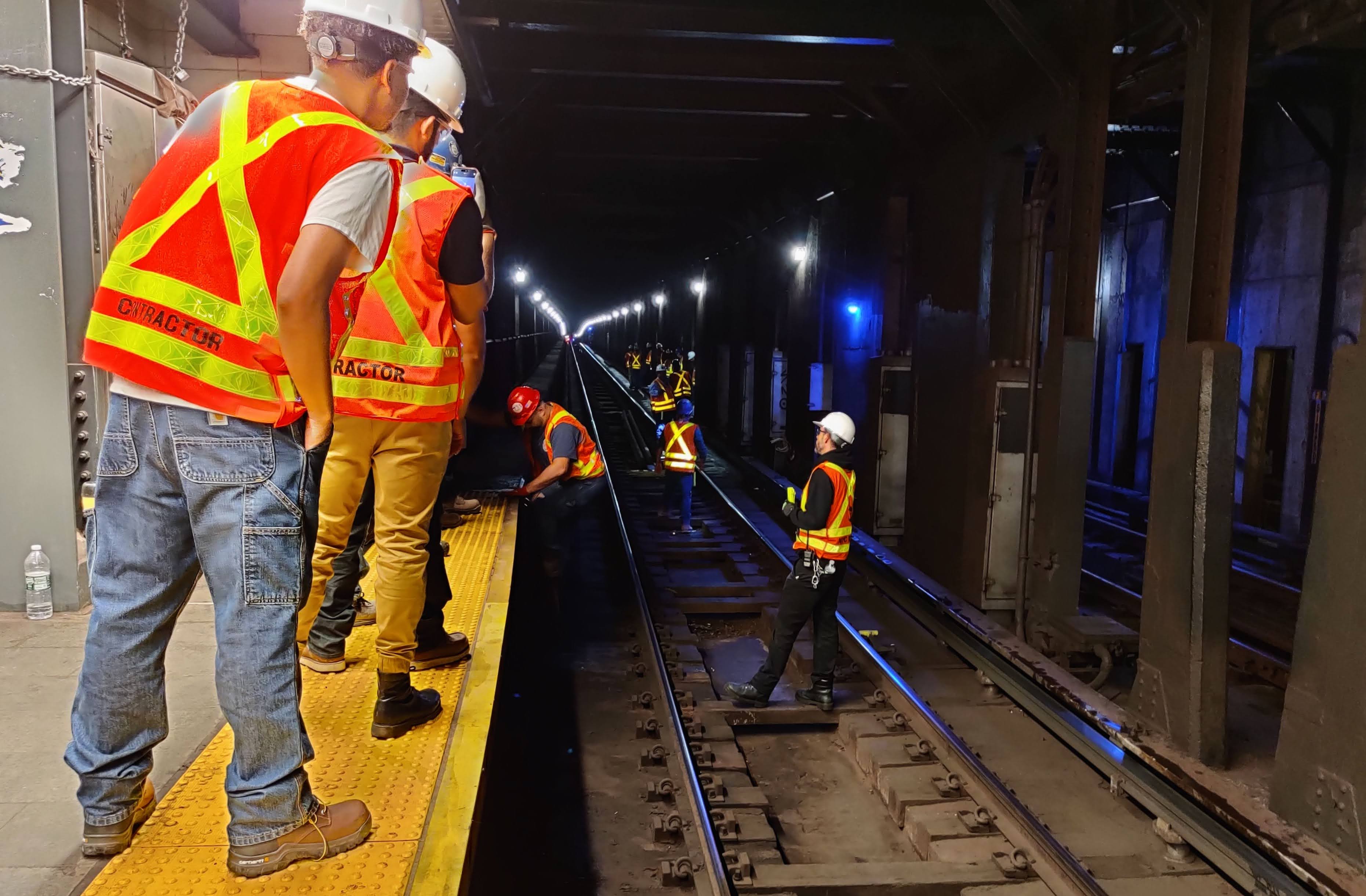 workers wearing high visibility vests climb down into the tracks.