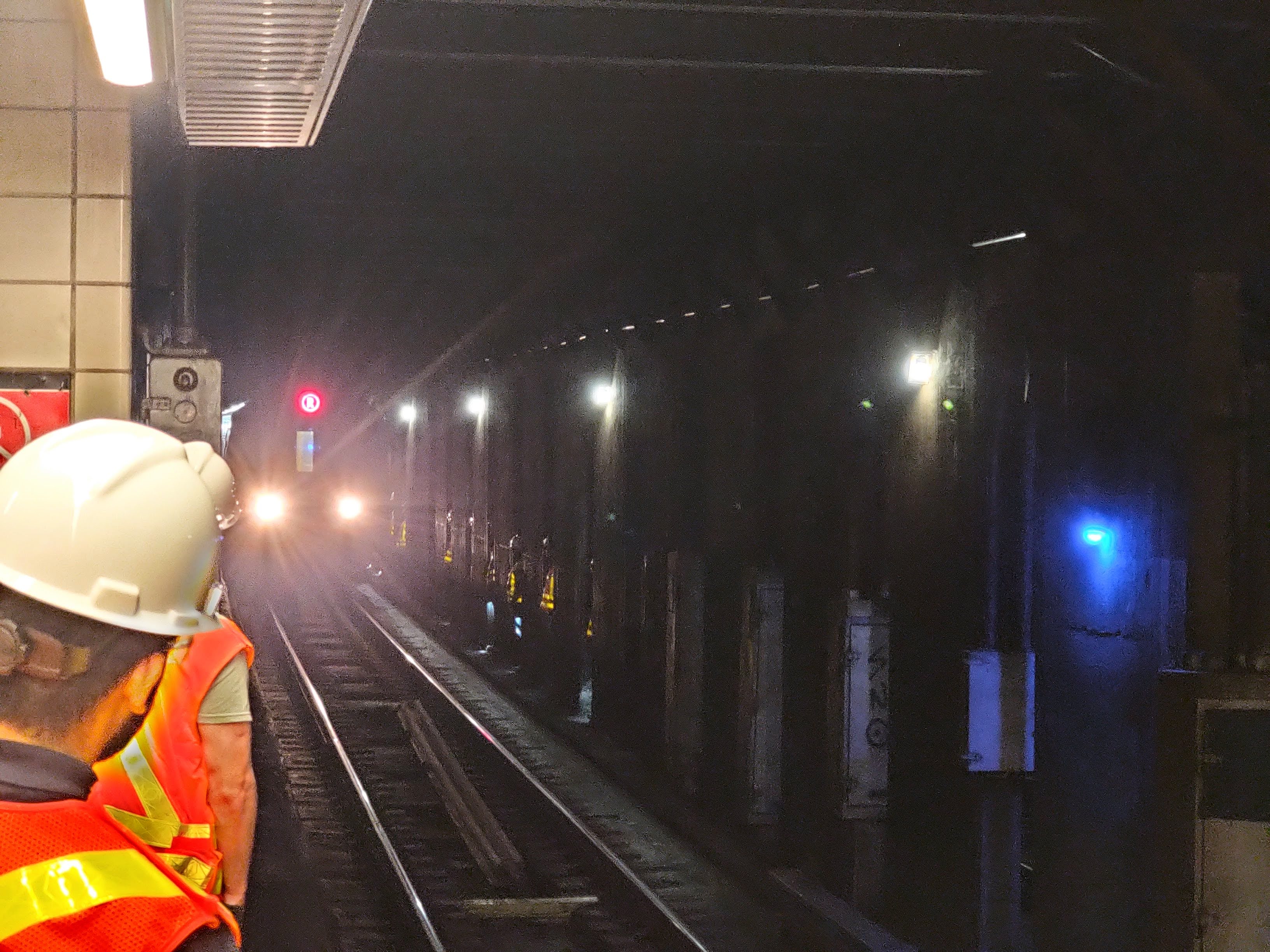 workers wearing high visibility vests watches train approaching.